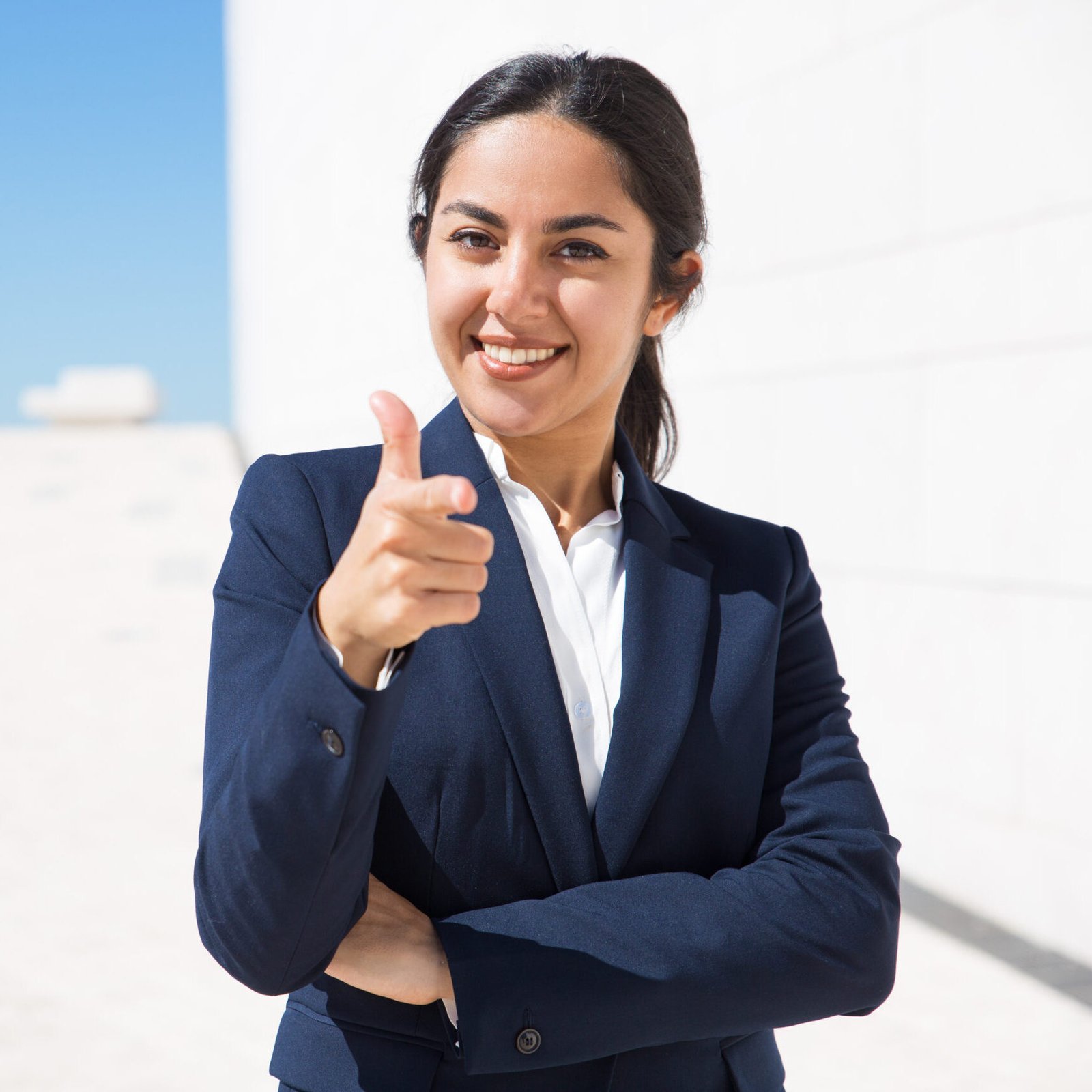 Happy ambitious HR manager choosing you. Confident young business woman in formal suit standing outside with arms folded and pointing finger at camera. Human resource or career concept