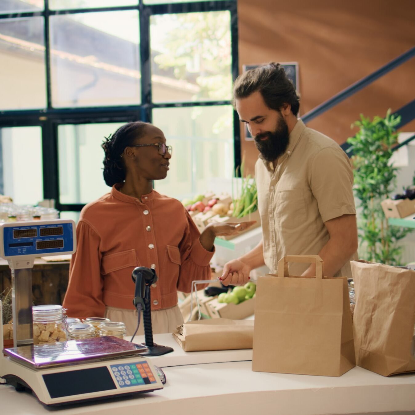 Seller assists customer in grocery store Seller assists customer in grocery store, recommending freshly harvested fruits and veggies on display. Couple searching for organic eco produce at local zero waste supermarket.